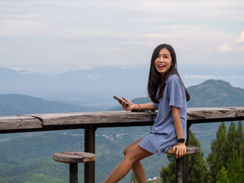 Portrait of young woman standing by railing against mountain