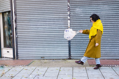 Young woman walking with plastic bottles in mesh bag on footpath