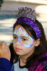 Cropped hand of parent painting daughter face during new year