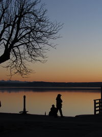 Silhouette people standing by lake against clear sky during sunset