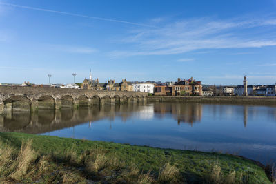 Bridge over river by buildings against blue sky