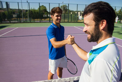 Male friends shaking hands while standing on tennis court