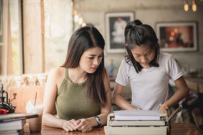 Girl with young woman using typewriter
