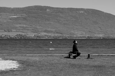 Woman sitting on shore by sea against sky