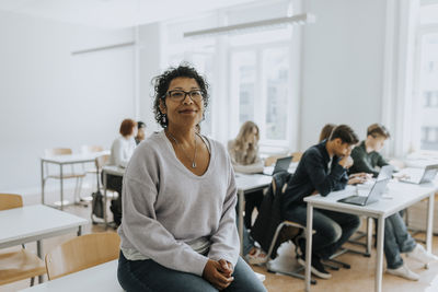 Portrait of female professor sitting on desk in classroom