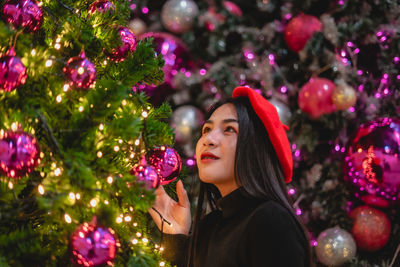 Close-up of beautiful young woman touching illuminated christmas tree