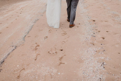 Low section of bride and groom walking at sandy beach