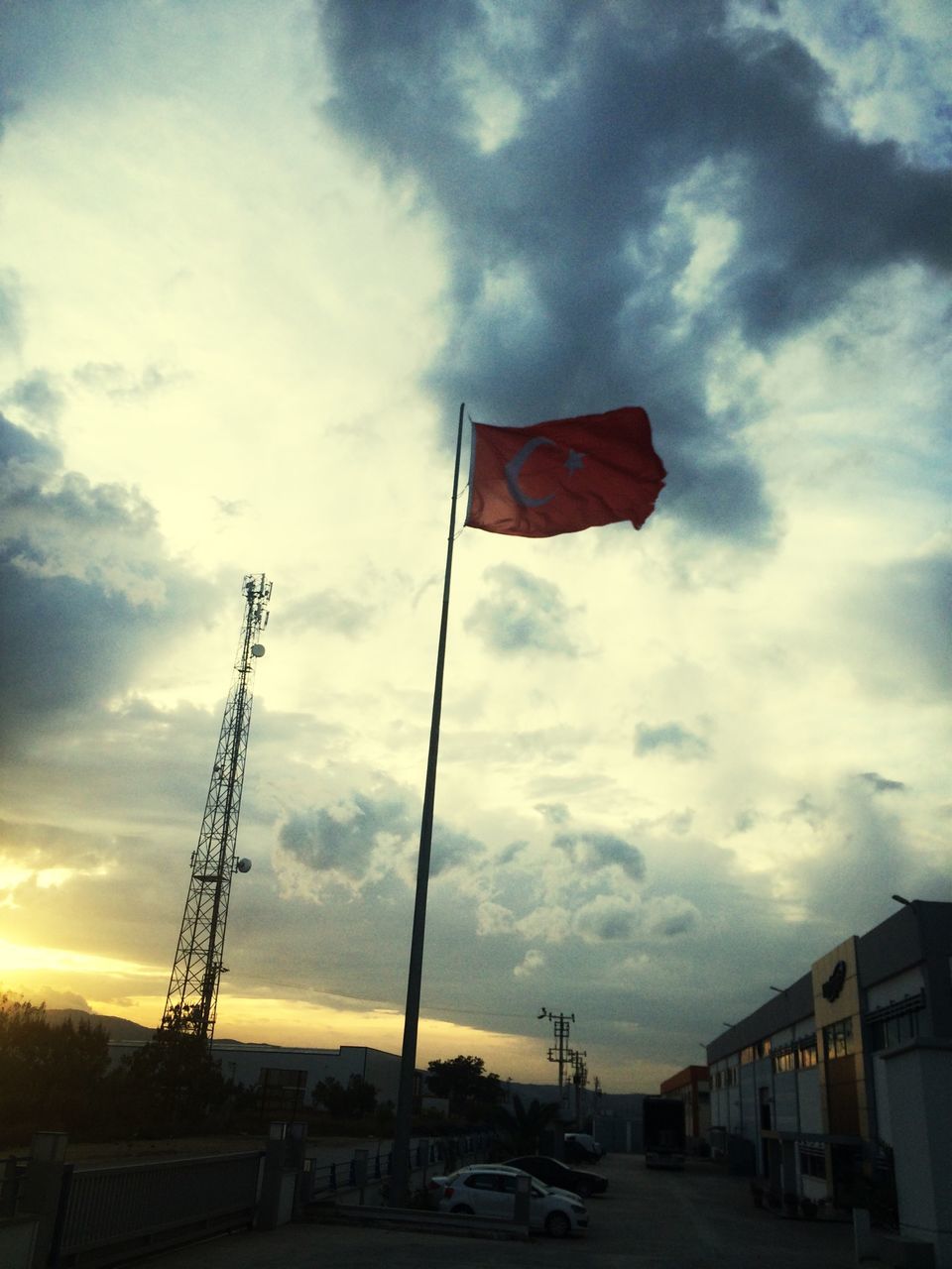 sky, architecture, building exterior, built structure, cloud - sky, cloud, flag, cloudy, transportation, street, low angle view, road, car, outdoors, land vehicle, city, sunset, no people, red, incidental people