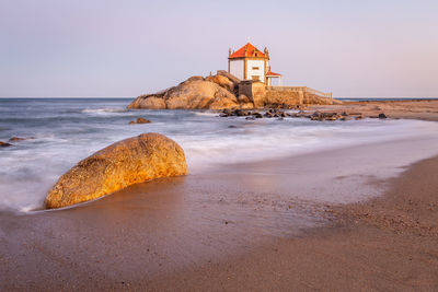 Lighthouse on beach by sea against sky