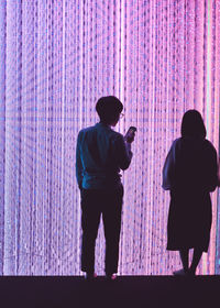 Rear view of man and woman standing against illuminated wall