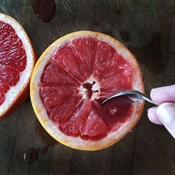 Cropped hand holding spoon over grapefruit on table