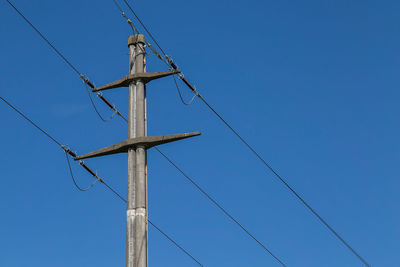 Low angle view of electricity pylon against blue sky