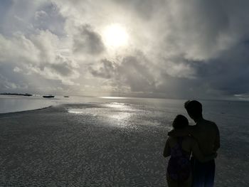 Rear view of men standing on beach against sky