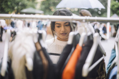 Young female customer buying dress hanging on rack at flea market