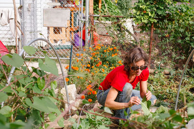 A woman in sunglasses picks vegetables in a flower-filled garden