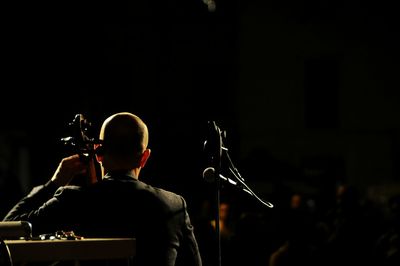 Rear view of man performing on stage at music concert