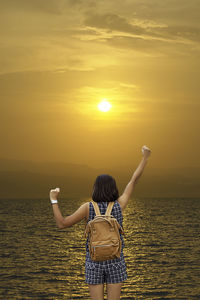 Rear view of woman in sea against sky during sunset