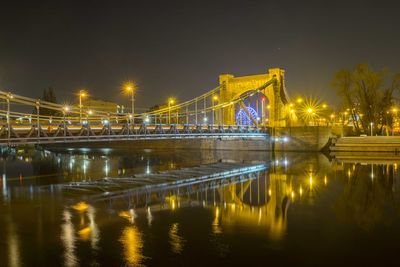 Illuminated bridge over river against sky at night