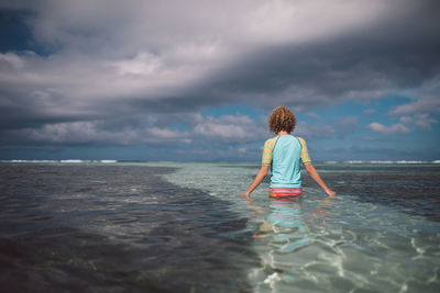Rear view of man looking at sea against cloudy sky