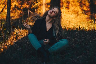 Young woman looking away while sitting on field
