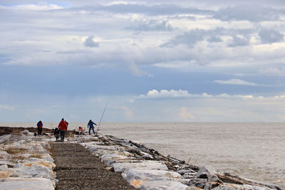 Rear view of people walking on beach by sea against sky