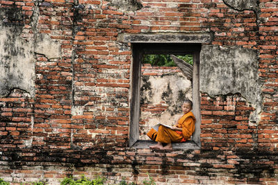 Monk reading book while sitting on entrance of old building