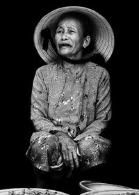 Senior woman wearing asian style conical hat while crouching against black background