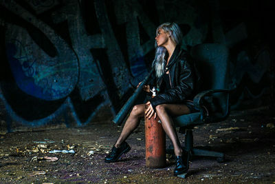 Full length of woman holding fire extinguisher while sitting on chair against wall