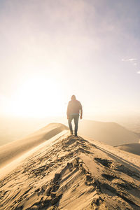 Rear view of man standing on sand dune against sky during sunset