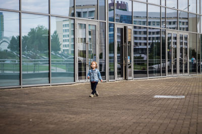 Girl walking on footpath by glass building