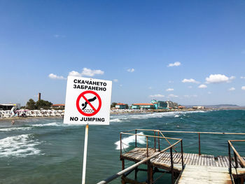 Warning sign by sea against sky