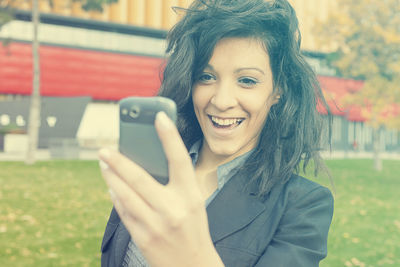 Close-up of smiling young woman using mobile phone at park in city