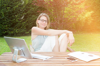 Portrait of smiling young woman with desktop computer sitting at park