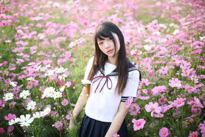 Beautiful young woman standing by pink flowering plants