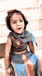 Cute girl in traditional clothing sitting on chair against wall