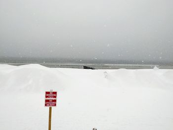 Road sign by sea against clear sky during winter