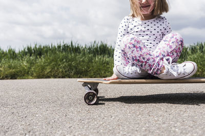 Girl sitting on road against sky