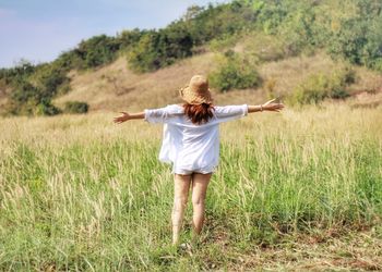 Rear view of woman with arms outstretched standing on field