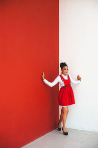 Full length of smiling girl standing against red wall