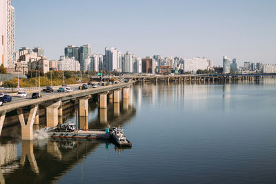 Boats in river by buildings in city against clear sky