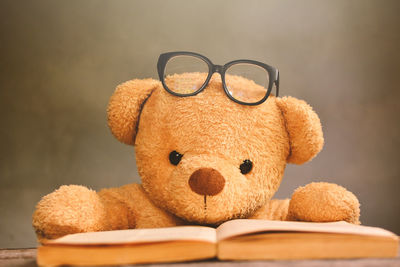 Teddy bear with eyeglasses by book on table against wall