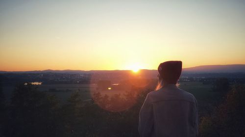 Rear view of silhouette woman standing on landscape during sunset
