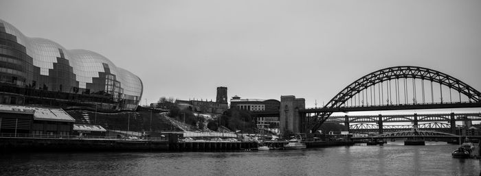 Bridge over river by buildings against sky