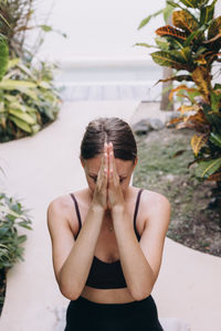 Portrait of  woman  sitting against tropical plants, with hand folded over the forehead 