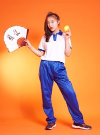 Portrait of smiling young woman standing against orange background