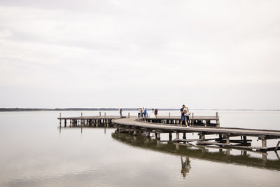 People on pier over sea against sky