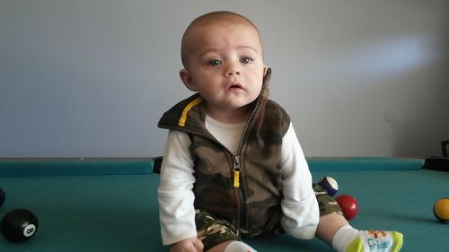 Portrait of cute boy sitting on pool table against wall