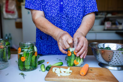 Process of canning a cucumber, senior woman canning fresh cucumbers with onion and carrots