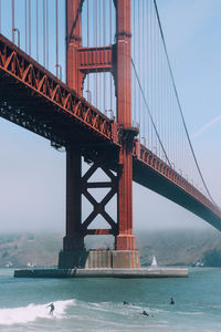 People surfing below golden gate bridge against sky