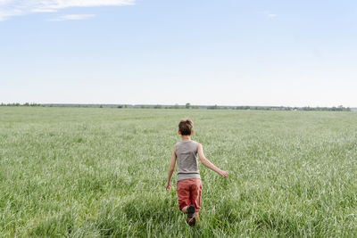 Boy running on grassy field by sky
